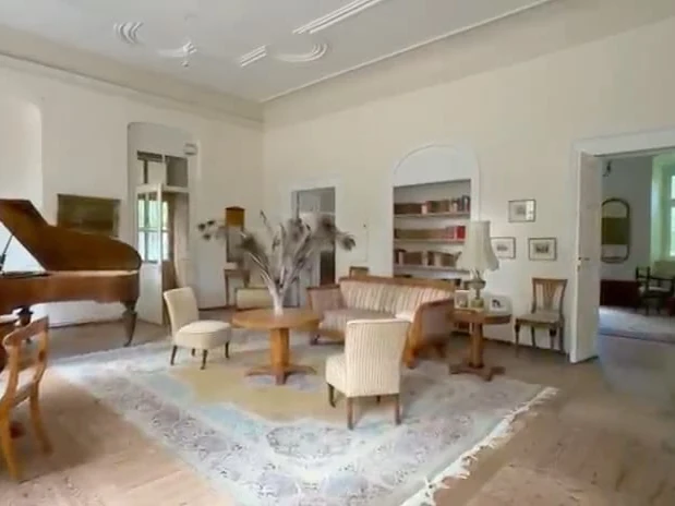 Salon avec piano à queue et fauteuils. Avant retouche.