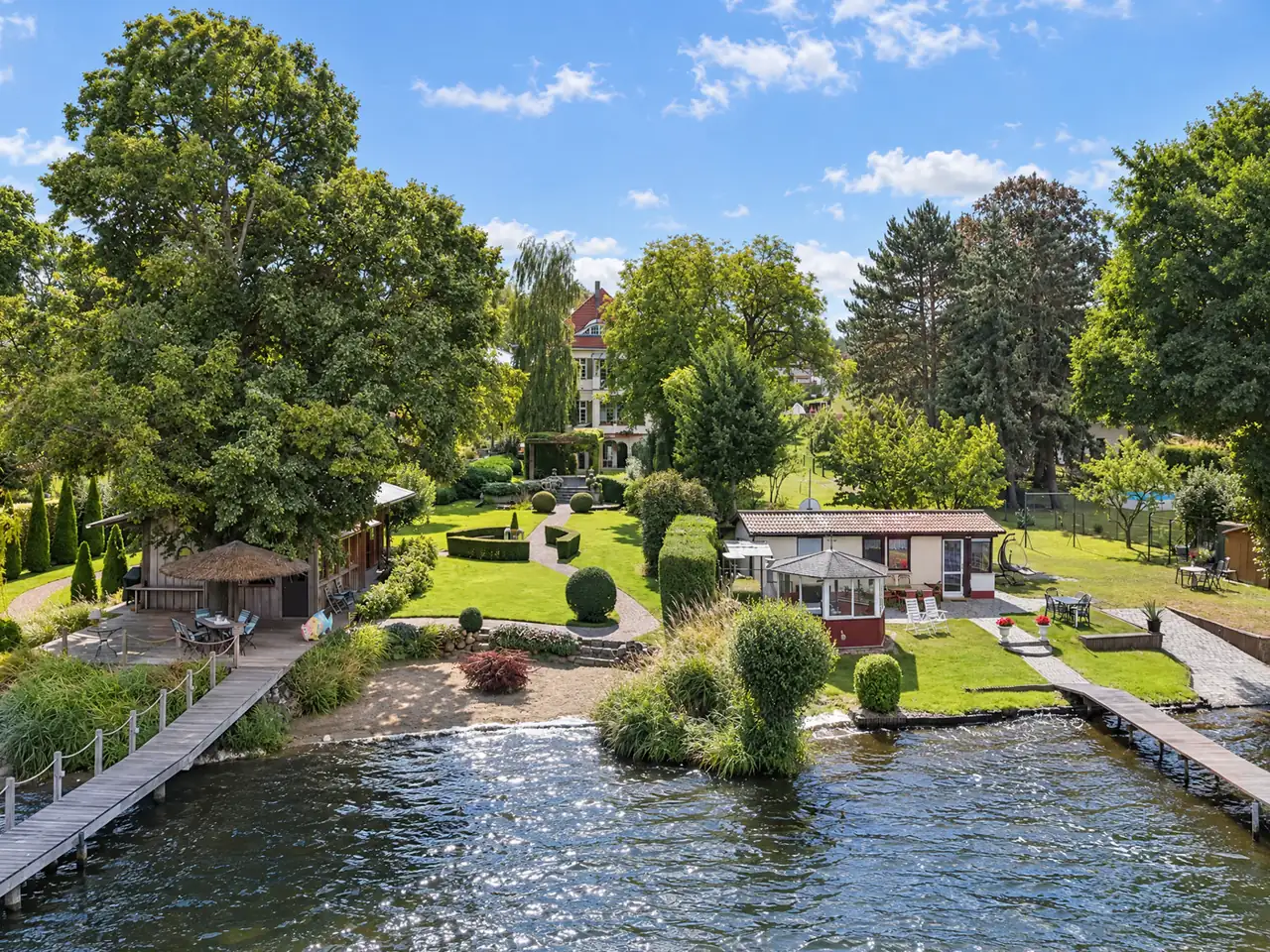 Vue de drone d'un bien au bord d'un lac, avec jardin et pontons. Après retouche.