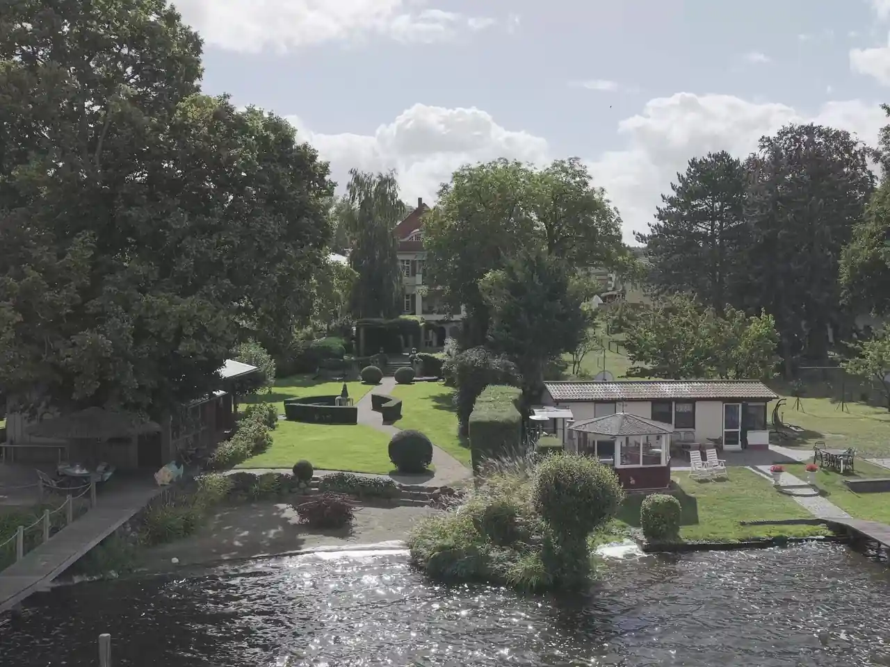 Vue de drone d'un bien au bord d'un lac, avec jardin et pontons. Avant retouche.